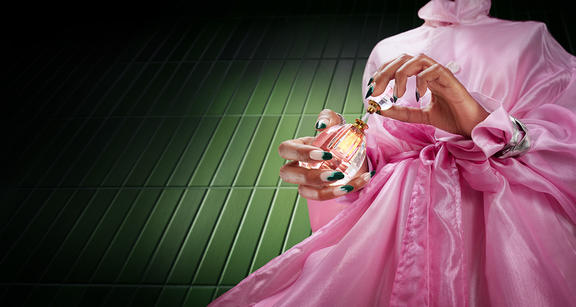 Woman in pink holding perfume bottle with manicured nails on green background